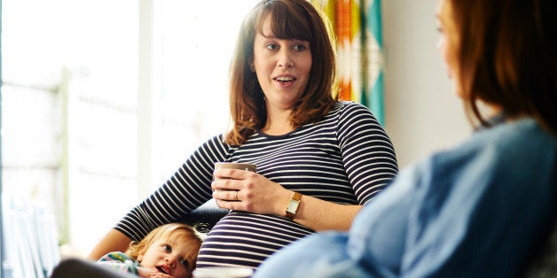 Pregnant women sitting with young daughter, chatting to pregnant friend with hot drinks