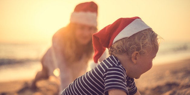 Little Santa helper playing in sand on the beach at the sunset