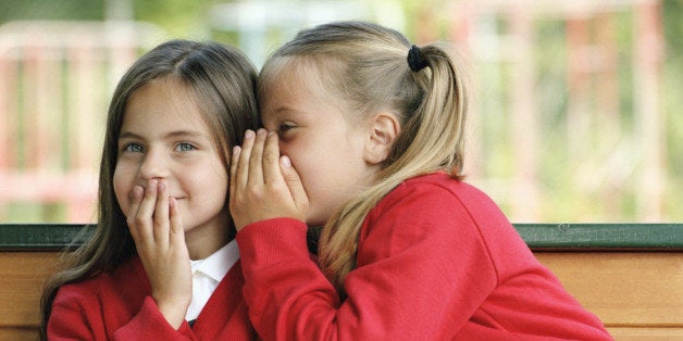 Two girls (6-8) sitting on bench whispering