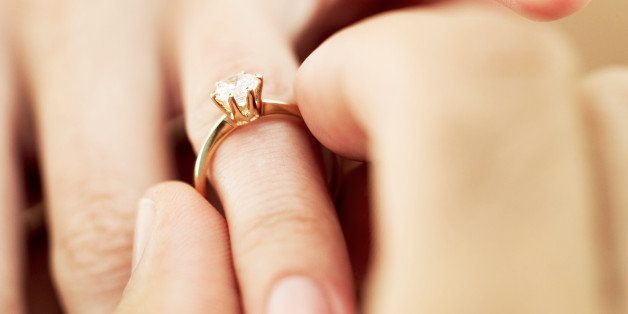 close-up of a man's hand putting a diamond engagement ring a woman's finger