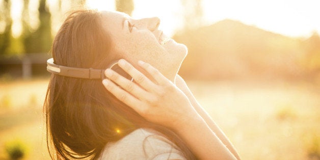 Young happy caucasian woman listening music in the nature with her modern ear phone, during the sunset.