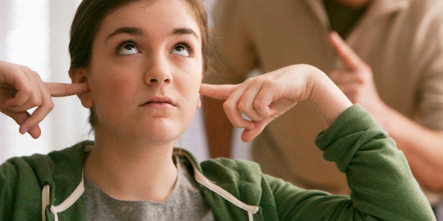 Daughter with fingers in ears as father scolds