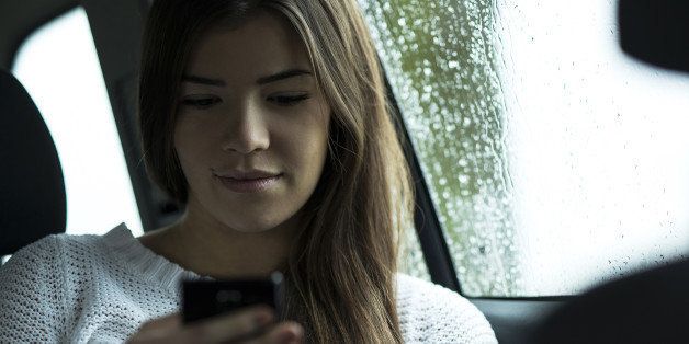 Young woman sitting inside car and looking at cell phone, on overcast day, Germany