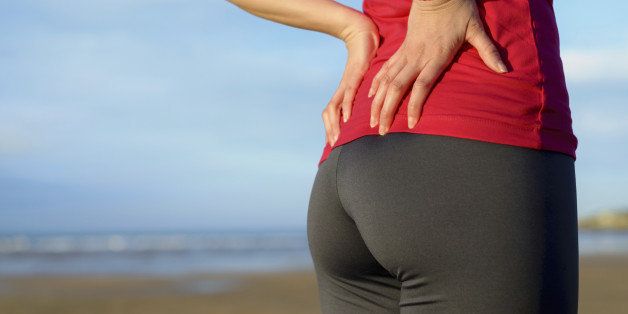Female athlete lower back painful injury. Caucasian fitness girl gripping her lowerback because sport injury after exercising and running.