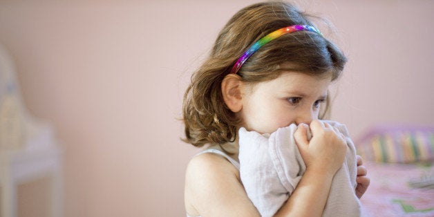 Unhappy three year old girl in bedroom holding comfort blanket to face