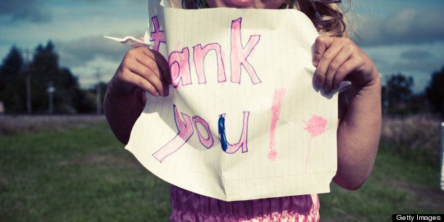 Little girl in pink fairy dress, holding up a child's drawn thank you sign.