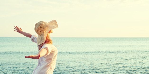 Happy beauty woman in hat is back opened his hands, relaxes and enjoys the sunset over the sea on the beach