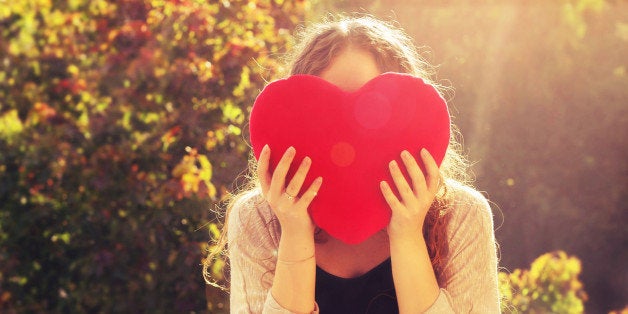 A girl holding up a heart in golden hour.