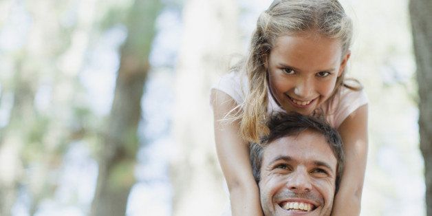 Smiling father carrying daughter on shoulders in woods