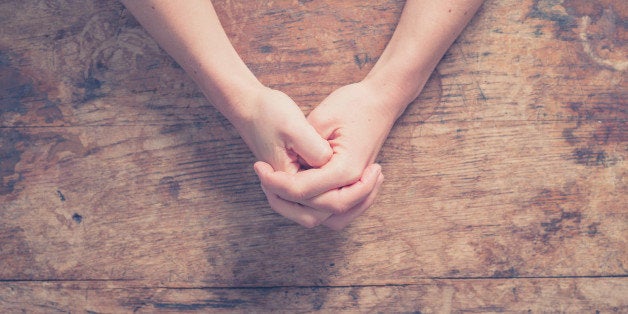 Close up on female hands folded in prayer at a wooden table