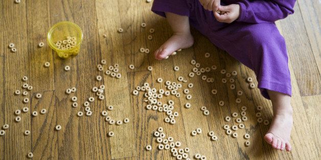 Young girl plays with cereal on the floor.