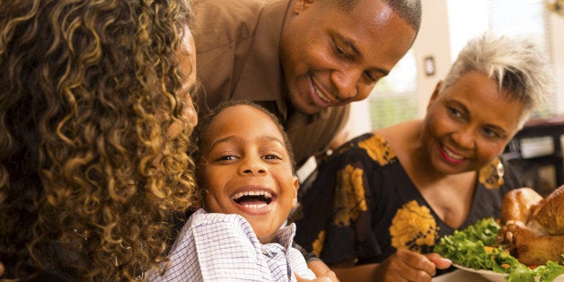 Family gathers together for Thanksgiving dinner. Mother is tickling son. Family laughs.