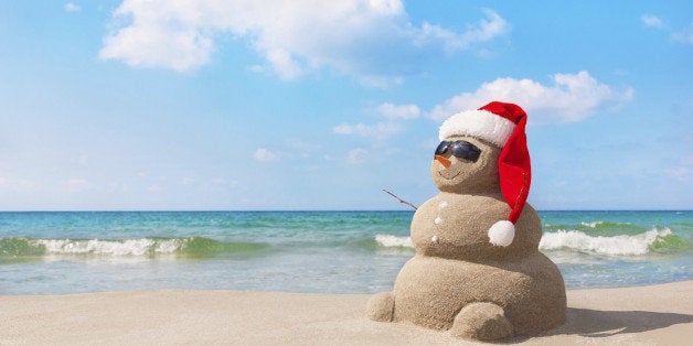 Sandy christmas snowman in red santa hat and sunglasses at sunny beach. Holiday concept for New Years Cards.