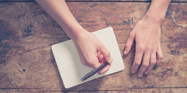 Close up on the hands of a young woman as she is writing in a small notepad at a wooden table