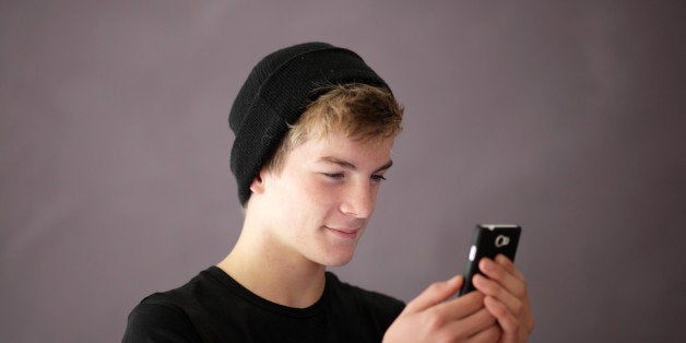 Teenage boy using his smartphone. He is smiling and wears a knitted cap.