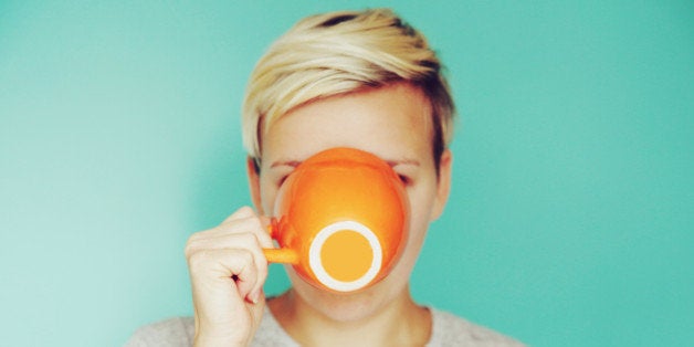 Young woman drinking out of an orange cup on a blue backdrop