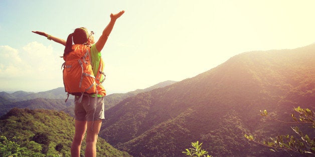 cheering woman hiker open arms at mountain peak cliff