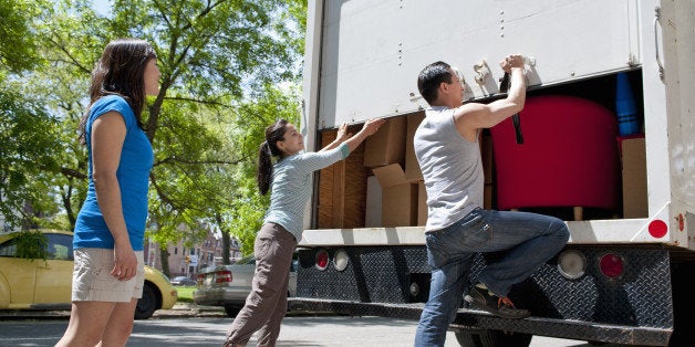 group of friends standing at the back of small moving truck, lifting up rear door, truck filled with moving boxes and furniture, urban environment