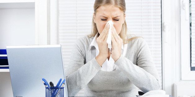 Young business woman sneezing while working in office