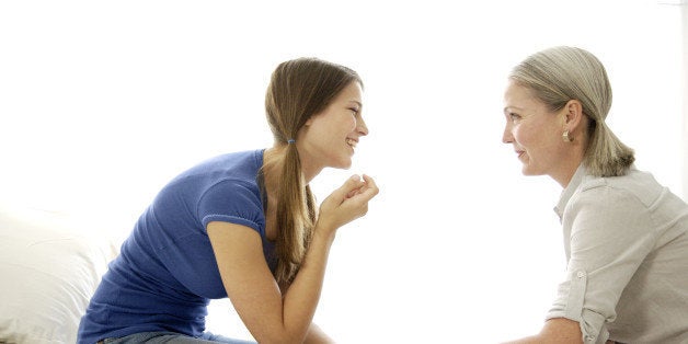 Mature mom and teenage daughter talking, bonding, and smiling with each other