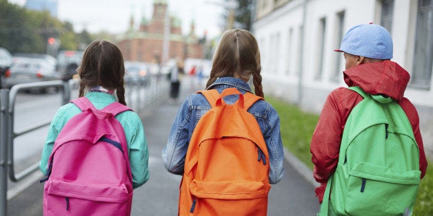 Backs of schoolkids with colorful rucksacks moving in the street