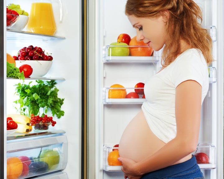 nutrition and diet during pregnancy. Pregnant woman standing near refrigerator with fruits and vegetables