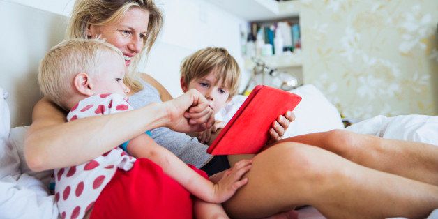 Mother with her sons watching tablet in bed