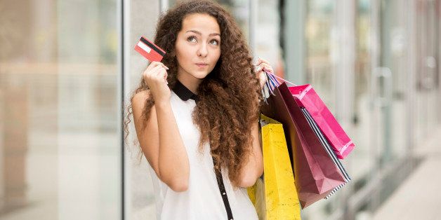 Pretty woman holding shopping bags and showing blank credit card, against mall background