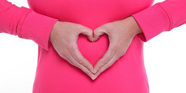 A woman making a heart shape with her hands over her stomach, concept of wellbeing and a healthy lifestyle.