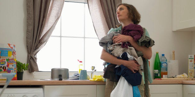 'Woman in kitchen holding laundry, looking careworn'