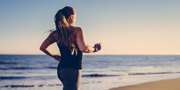 Long blond haired woman jogging at beach with smartwatch into sunlight.
