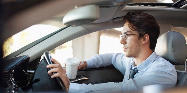 Businessman holding coffee cup and driving car