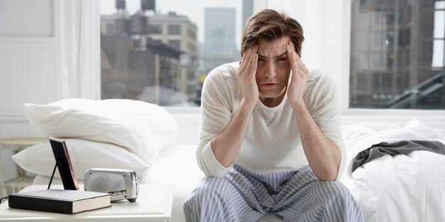 Young man sitting on bed and rubbing forehead