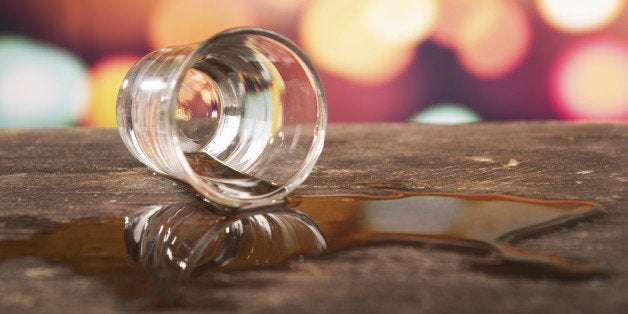 glass of rum whiskey alcohol on wooden table over defocused lights background