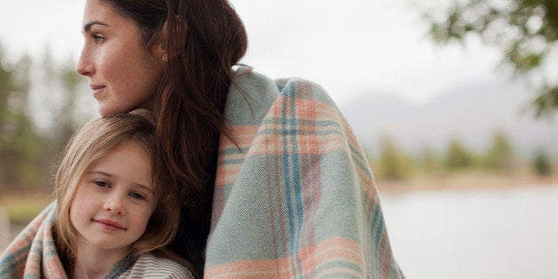 Portrait of smiling daughter wrapped in blanket with mother at lakeside