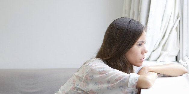 Profile portrait of a young woman sitting alone looking out window