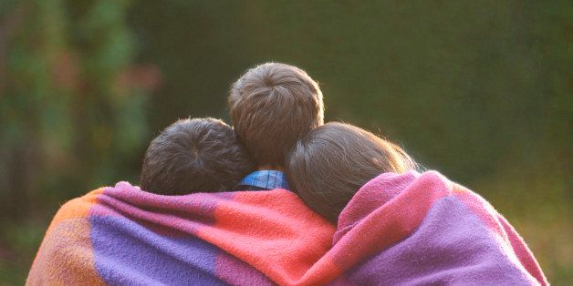 Siblings wrapped in blanket in garden