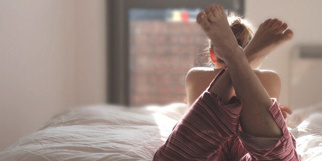 Young woman laying on the bed in the sunshine, legs crossed, soft light. 