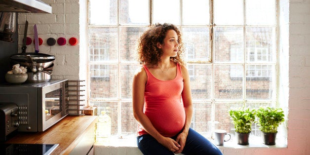 A pregnant lady sits in her modern kitchen window looking thoughtful on a sunny day