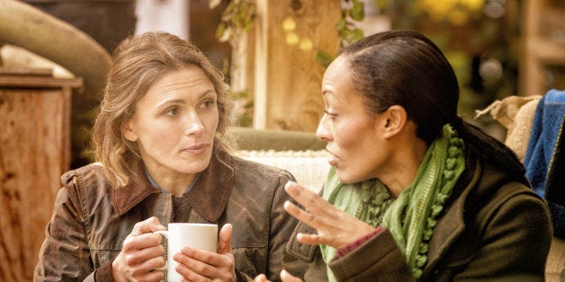 Two female friends discussing over a cup of coffee. They are sitting outdoors in Autumn. Halloween pumpkins can be seen in the foreground.