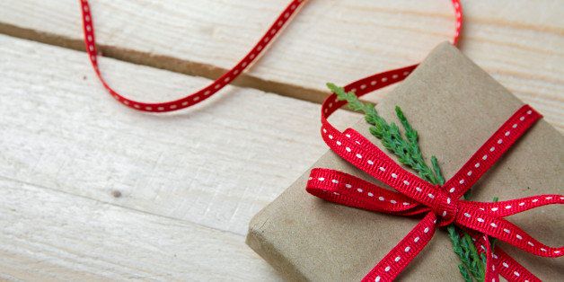 Gift box, wrapped in recycled paper and red bow on wood background