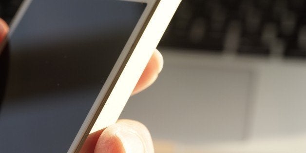 Social media. Female hand holding a mobile phone in front of computer laptop, downloading images ready to upload to a social network site. Space for copy.