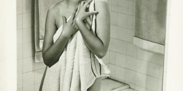 Mirror with reflection of woman covering herself with towel in bathroom, (B&W), portrait