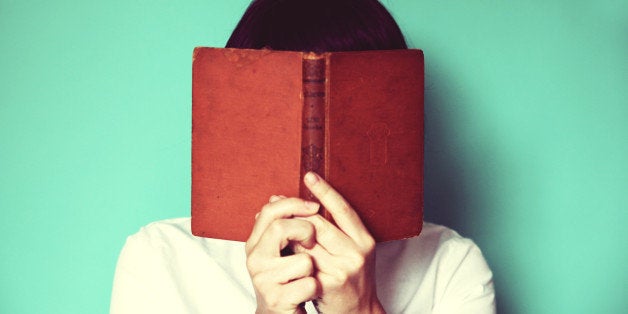 Woman's holding a book in front of her face.