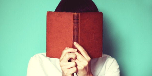 Woman's holding a book in front of her face.