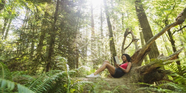 USA, Oregon, Portland, Young woman reading book on log in forest