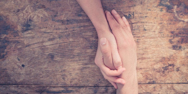 Close up on a man and a woman holding hands at a wooden table