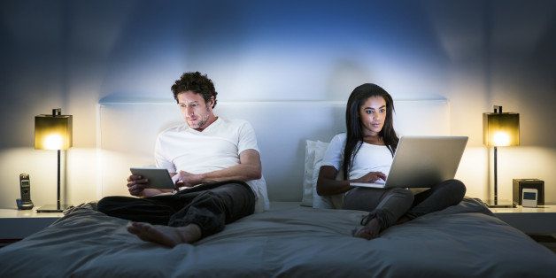 Multi-ethnic couple using technologies in bedroom at home