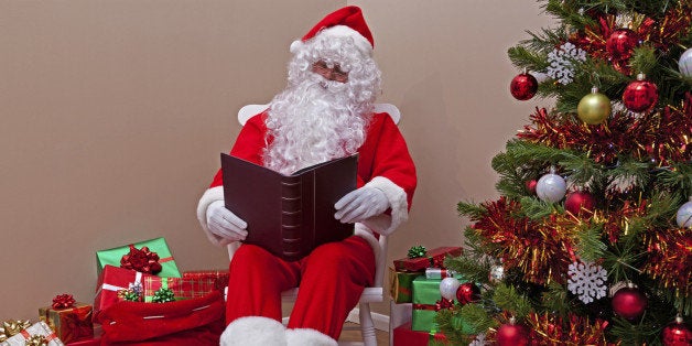 Santa Claus sat in a rocking chair reading the 'naughty or nice' list surrounded by gift wrapped presents.