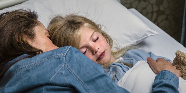 Mom caressing her sleeping child in a hospital bed.